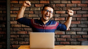 Blog Post Hero: a young man on his computer celebrating success
