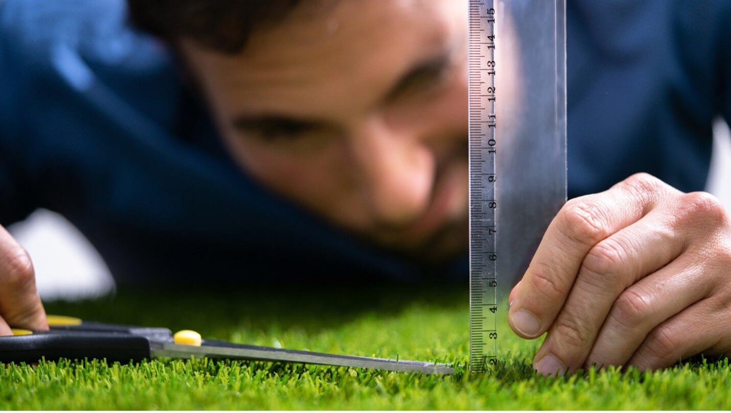 a man measuring the grass and cutting it with a scissors