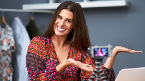 Blog Post Thumbnail: A cheerful woman with long brown hair wearing a colorful patterned top presenting to a camera, showcasing a product or concept with a bright smile.