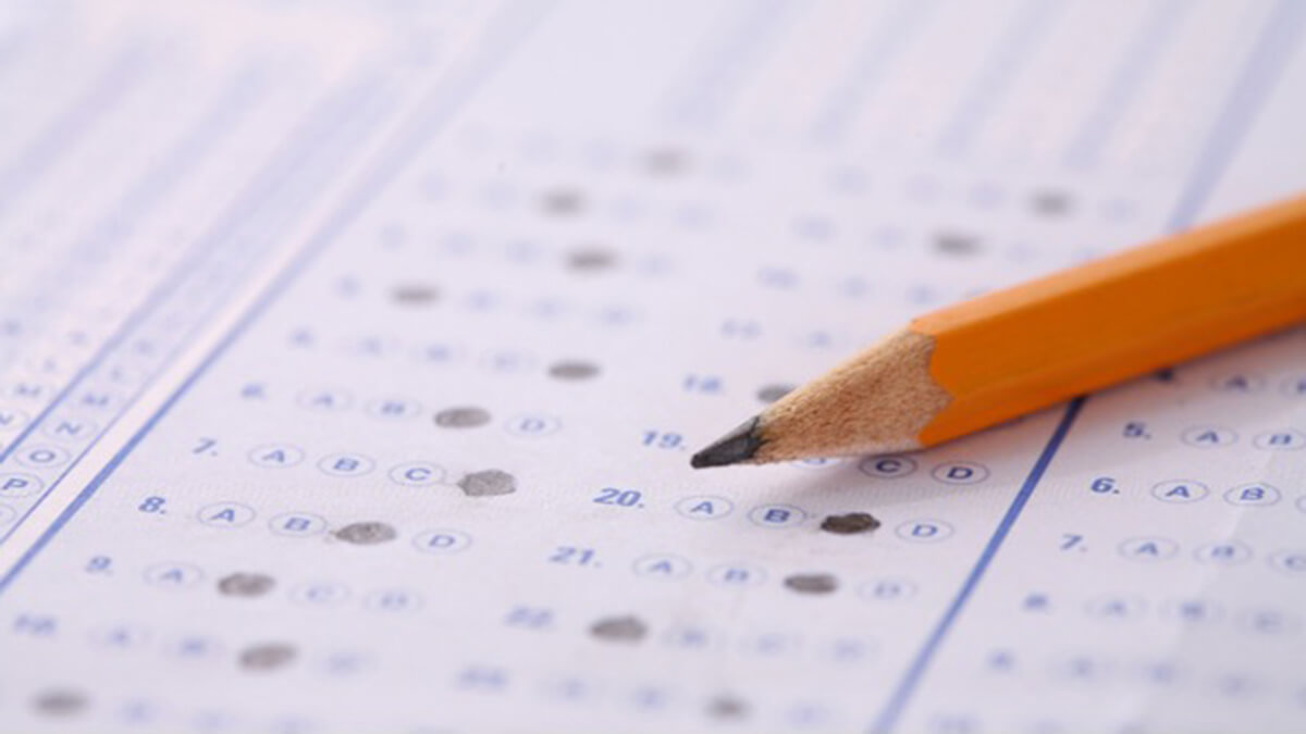  close-up of a standardized test answer sheet with multiple-choice questions, filled in with pencil marks. A yellow pencil with a pointed tip rests on the sheet, indicating either a pause in answering or the completion of the test.
