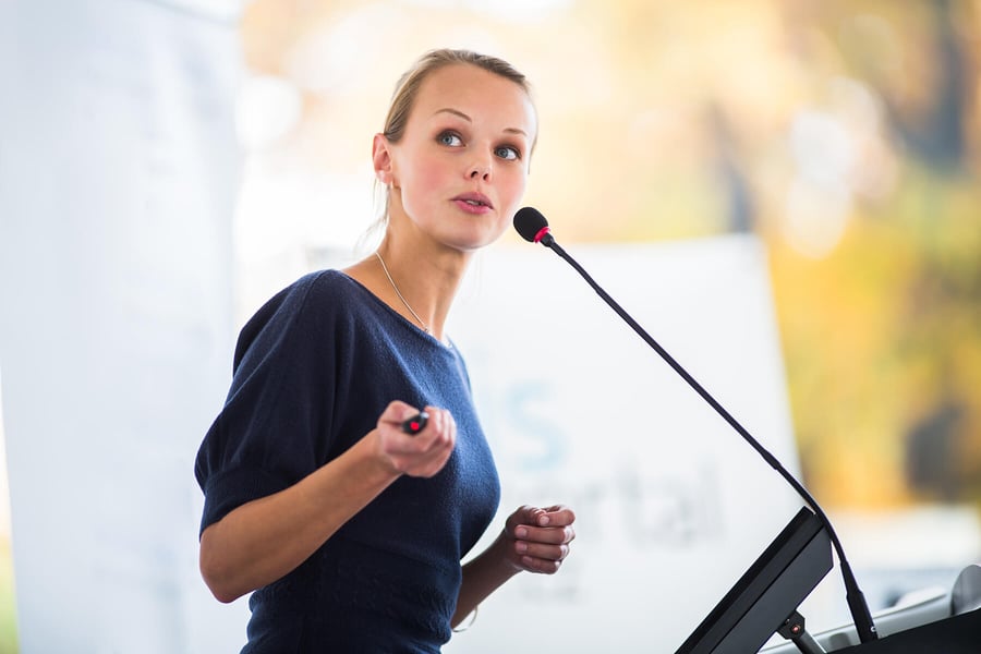 Blog Post Hero: a woman speaking at a podium